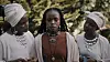 Marima Wanjiru as Anam stands between two women dressed in white headwraps and layered jewelry in a still from the Kenyan psychological thriller Anam’s Wake.