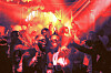 A crowded dance floor lit by red lights and spotlights, with people moving and raising their arms.