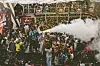 Large crowd in a stadium with confetti and smoke during a celebration.