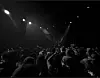 Crowd standing in a dark concert venue beneath bright stage spotlights.