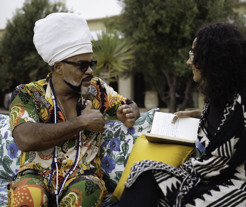 A Brazilian man in colorful clothes is sitting on a bench with a young woman in deep conversation.
