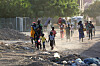 People walk and carry belongings along a dusty, debris-strewn street in Khartoum as they flee fighting.