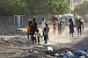 People walk and carry belongings along a dusty, debris-strewn street in Khartoum as they flee fighting.
