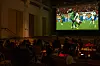 Crowd seated in a dark venue watches Morocco vs Senegal on a large screen at BASE Milano in Milan.