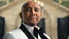 Portrait of a man in a black tuxedo standing before a blurred building exterior.