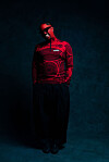 Person in red-lit studio wearing patterned top, sunglasses, and black wide-leg pants.