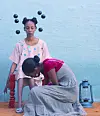 Hiba Elgizouli is sitting on a small stool wearing a pink dress with blue dots while her sister Sally is fixing her shoes, which are blue with pink dots.