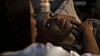 S'dumo Mtshali lies in bed in a dimly lit scene, with another person blurred in the foreground.