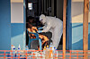 A worker in protective suit takes samples from a patient seated in a doorway at an Ebola treatment center.
