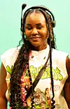 Portrait of a person with long braided hair wearing headphones and a graphic shirt on a mint green background.