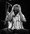 Black-and-white image of a seated musician with hands on his face next to a microphone.