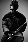 Black-and-white portrait of musician Linda Sikhakhane seated, holding a saxophone against a plain background.