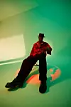 Person seated in a chair under green and orange studio lighting.