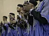 A line of Gnaoua musicians in blue traditional attire is clicking their qraqeb.
