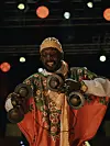 A man wearing a red-and-green jellaba is moving while playing the qraqeb.