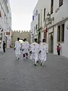 Four Moroccan men in traditional white attire are walking away from the camera in the medina of Essouira.