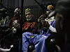 Five men are sitting on the floor in front of microphones, playing instruments and wearing colorful traditional Moroccan attire.