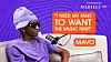 A man in purple clothing sits on a couch next to a microphone and an orange sign reading Mavo.