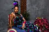 NALEDI poses in a black dress with blue, purple and lilac embellishments and surrounded by Zulu cultural artefacts.