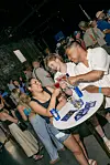 Crowd at a Martell event table with drinks, brochures and branded items in a busy indoor venue.