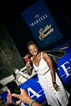 Person in white holding a cocktail next to a blue Martell-branded vehicle and banner.