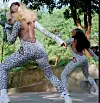 Two dancers in leopard-print bodysuits perform energetic poses outdoors near a low wall and trees.
