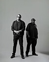 Two men standing in a black-and-white studio portrait against a plain background.