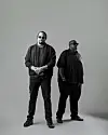 Two men standing in a black-and-white studio portrait against a plain background.