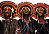 Wodaabe men in ceremonial dress and elaborate yellow and black facial makeup during Niger's Gerewol courtship festival, smiling beneath large woven hats as part of a traditional beauty dance.