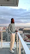 Person standing on a rooftop terrace with a city skyline and cloudy sky behind.