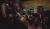 A group of people in colorful clothing and headwraps gathered closely indoors.