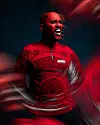 Man in a red shirt standing against a dark background with swirling red motion blur.