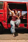 Zee Nxumalo poses in a red minibus taxi. She wears a red top and stylish blue jeans.