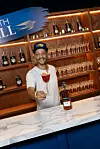 Marcio Ramos is presenting a red cocktail and a Martell bottle behind a bar with illuminated shelves.