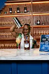 Thandi Walton shakes a cocktail beside a Martell bottle at a bar with backlit shelves and glassware.
