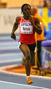 Zambian runner Racheal Nachula sprints indoors wearing a red Zambia jersey and bib number 8.