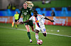 Two women’s football players sprint after the ball during a UEFA Champions League match on a green pitch.