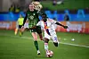 Two women’s football players sprint after the ball during a UEFA Champions League match on a green pitch.