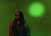 Person with long hair and glasses lit by red and green light against a green background.