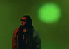 Person with long hair and glasses lit by red and green light against a green background.