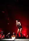 A singer performs on a red-lit stage while people stand near the front in the foreground.