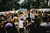 A dense crowd gathers outdoors near a brightly lit stage at a music festival.