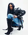 Abigail Chams in a black leather jacket, jeans, and black boots seated against a white background.