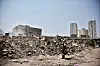 Security officer stands beside a large rubble pile in Cairo with high-rise towers in the distance.