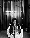 Black-and-white portrait of Adey seated, wearing a white embroidered outfit, with long locs draped over her shoulders and her hands in front of her face.
