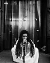 Black-and-white portrait of Adey seated, wearing a white embroidered outfit, with long locs draped over her shoulders and her hands in front of her face.