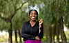 Jalisa Whitley smiles in a black blouse and bright pink trousers, standing against a backdrop of trees.