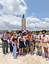 A group of women poses in Ghana holding copies of Yaa Gyasi’s Homegoing, with a large monument behind them.