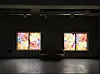 Dark gallery featuring two colorful illuminated artworks, chairs, and a reflective floor.
