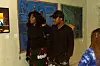 Two visitors stand in a gallery beside colorful wall-mounted textile artworks.